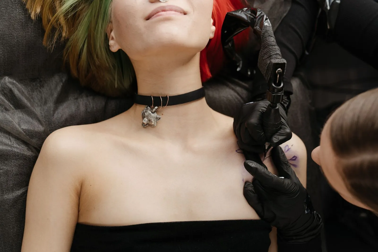 Asian woman with colored hair receiving a tattoo on shoulder in a studio.